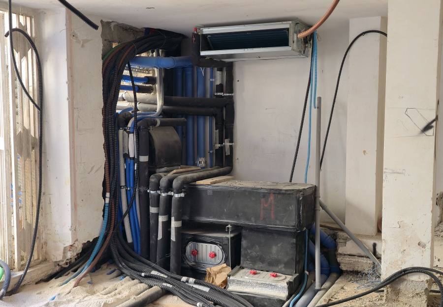 Nodo di distribuzione in cantiere: tubazioni coibentate, ventilconvettore canalizzato a soffitto e plenum di mandata con serrande