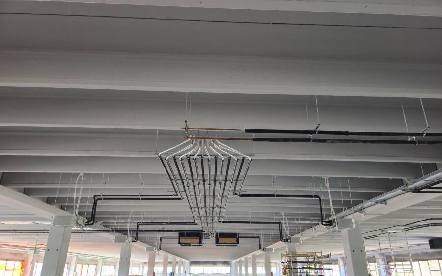 Capannone industriale con impianto di climatizzazione VRF in corso di realizzazione: linee frigorifere a ventaglio dal collettore e unità interne a soffitto
